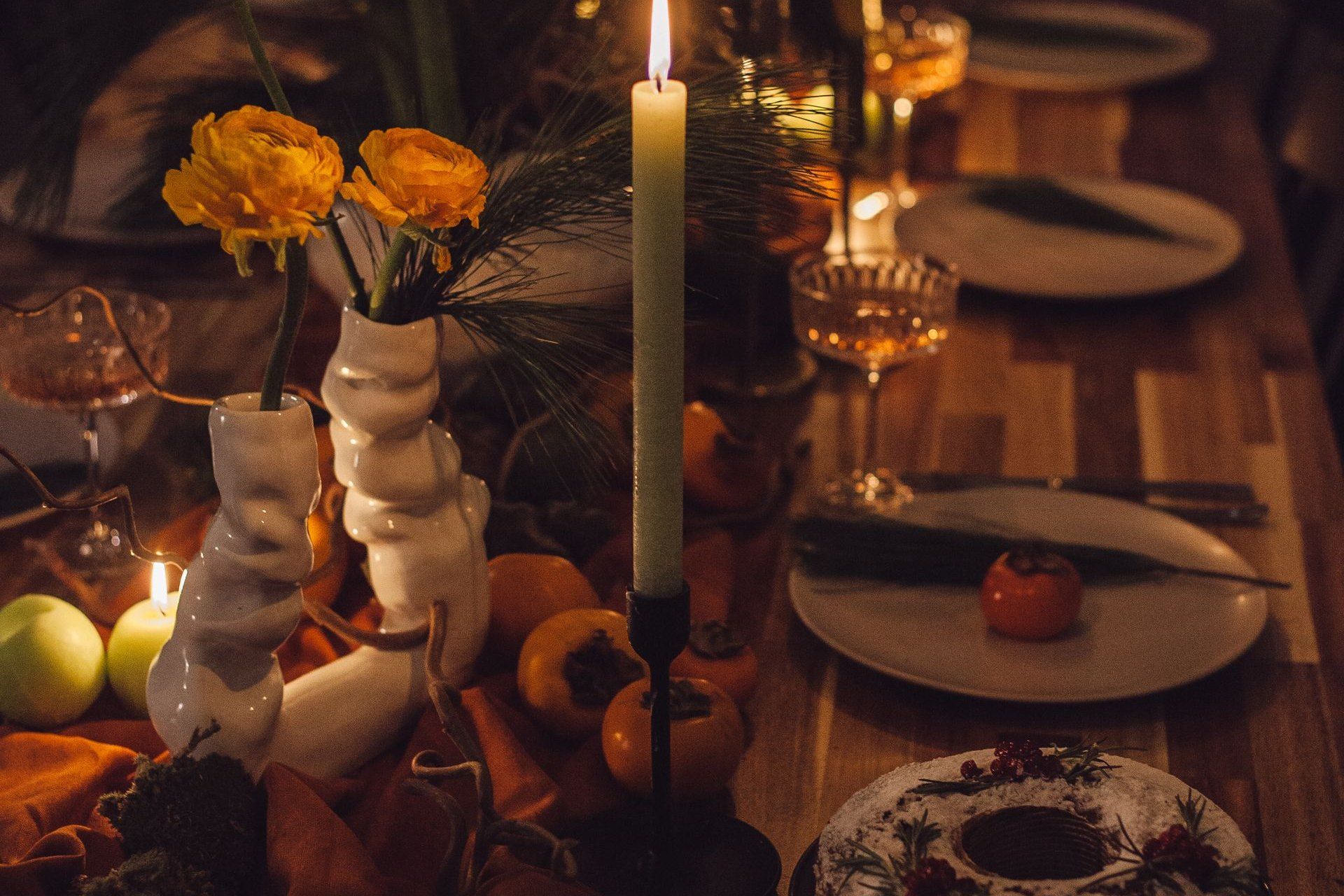 Gedeckter Holztisch am Abend mit brennender Kerze, Blumen und Tellern