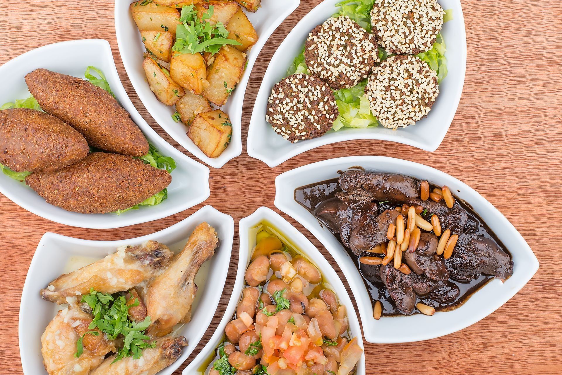 Vorspeisen in weißen Schalen von oben: Kibbeh, Falafel, Kartoffeln und Bohnen